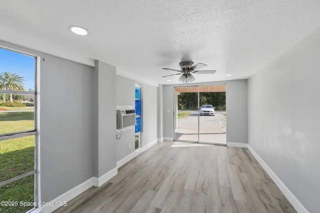 a view of a hallway to a livingroom with wooden floor a ceiling fan and windows