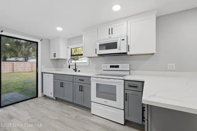 a kitchen with stainless steel appliances granite countertop white cabinets a sink a stove a microwave and a refrigerator