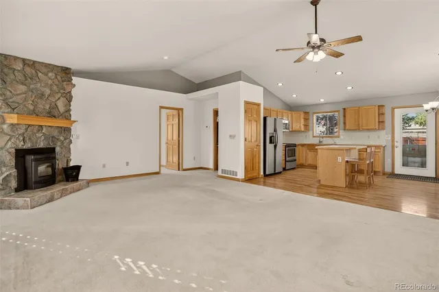 a view of a livingroom with a fireplace a ceiling fan a kitchen view and a window