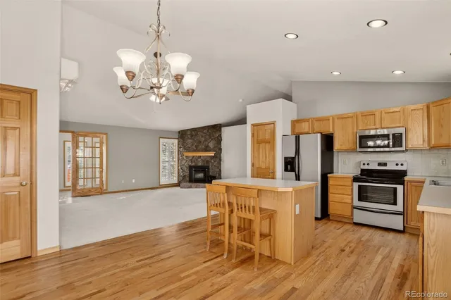 a view of a kitchen with stainless steel appliances granite countertop a stove top oven a refrigerator a dining table and chairs with wooden floor