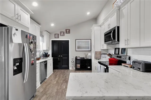 a kitchen with stainless steel appliances kitchen island granite countertop a refrigerator oven a stove top oven a sink dishwasher and white cabinets with wooden floor