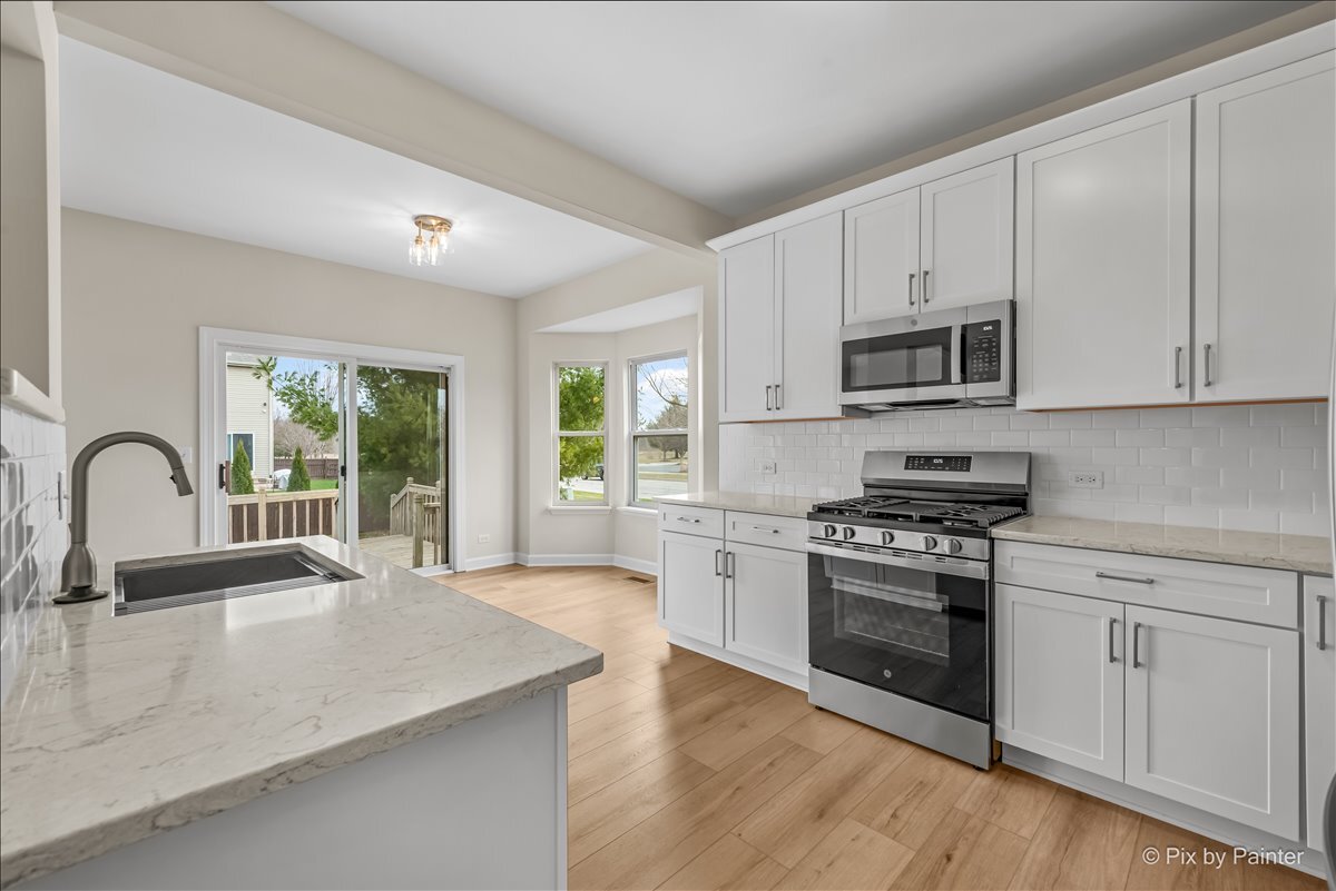216 Winding Trail Genoa, IL 60135 - Photo 15 of 52 a kitchen with stainless steel appliances granite countertop a stove a sink dishwasher a microwave oven with a dining table and chairs with wooden floor