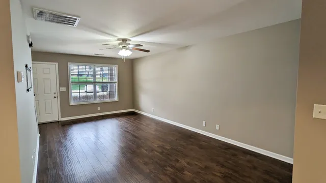 an empty room with wooden floor chandelier fan and windows