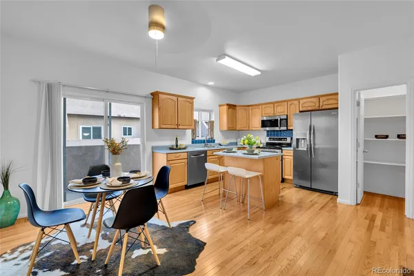 a kitchen with stainless steel appliances kitchen island granite countertop a refrigerator a stove a sink dishwasher and a dining table with wooden floor