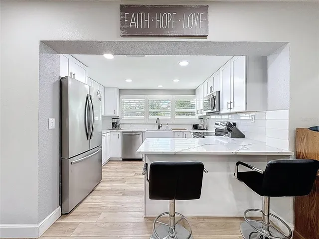 a kitchen with stainless steel appliances granite countertop white cabinets a sink a stove a microwave and wooden floors