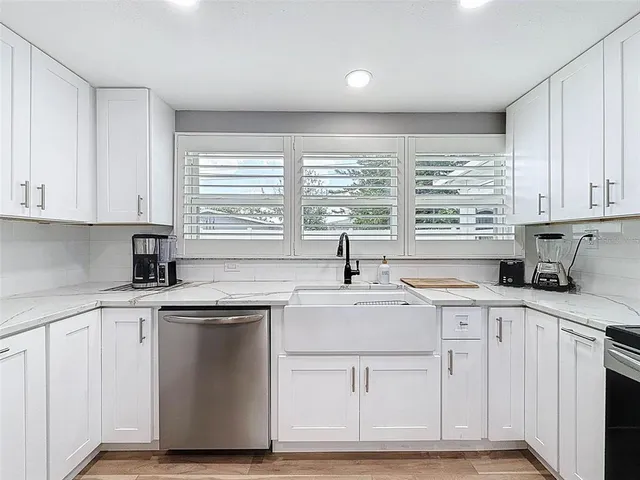 a kitchen with stainless steel appliances a sink dishwasher a stove top oven a refrigerator with white cabinets and wooden floor