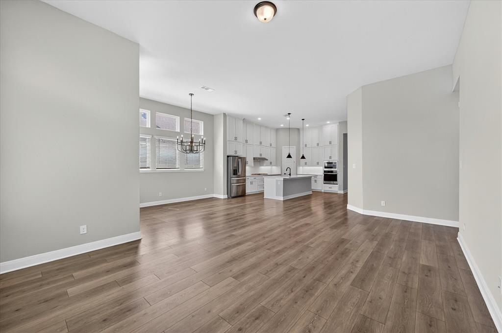 2237 Pika Road Northlake, TX 76247 - Photo 7 of 37 Spacious open-concept interior featuring wood-finish flooring, light gray walls, a contemporary kitchen with a center island, stainless steel appliances, and abundant white cabinetry