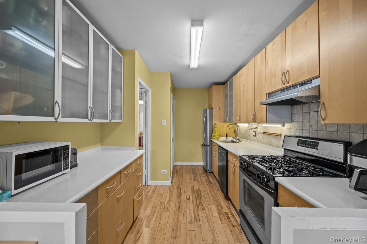 2500 Johnson Avenue North, Unit 2NP Bronx, NY 10463 - Photo 13 of 45 Kitchen with glass insert cabinets, appliances with stainless steel finishes, light wood finished floors, under cabinet range hood, and decorative backsplash