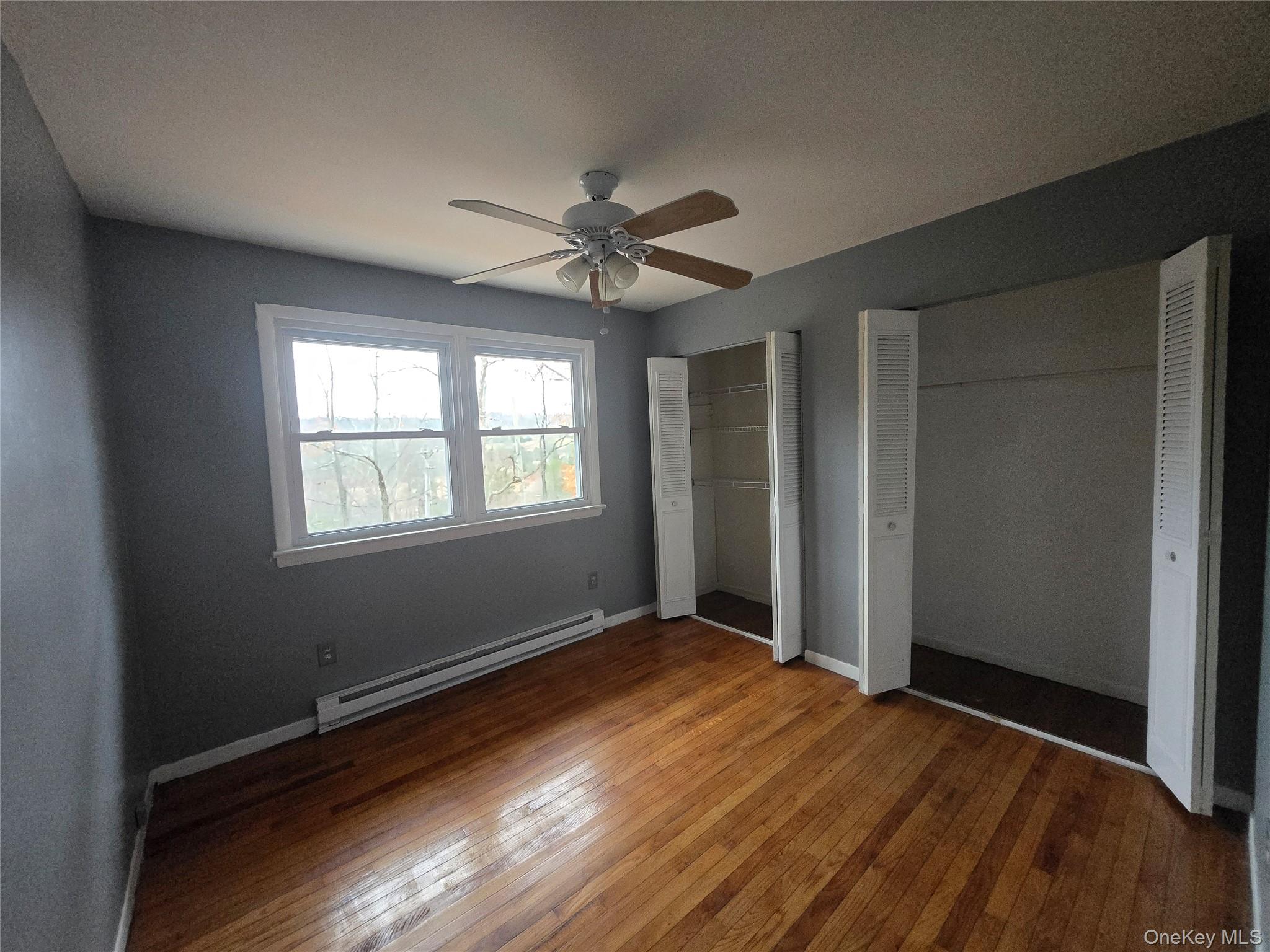 43 Glenmere Homesites Road Florida, NY 10921 - Photo 11 of 30 Unfurnished bedroom featuring two closets, a baseboard heating unit, hardwood / wood-style floors, and a ceiling fan