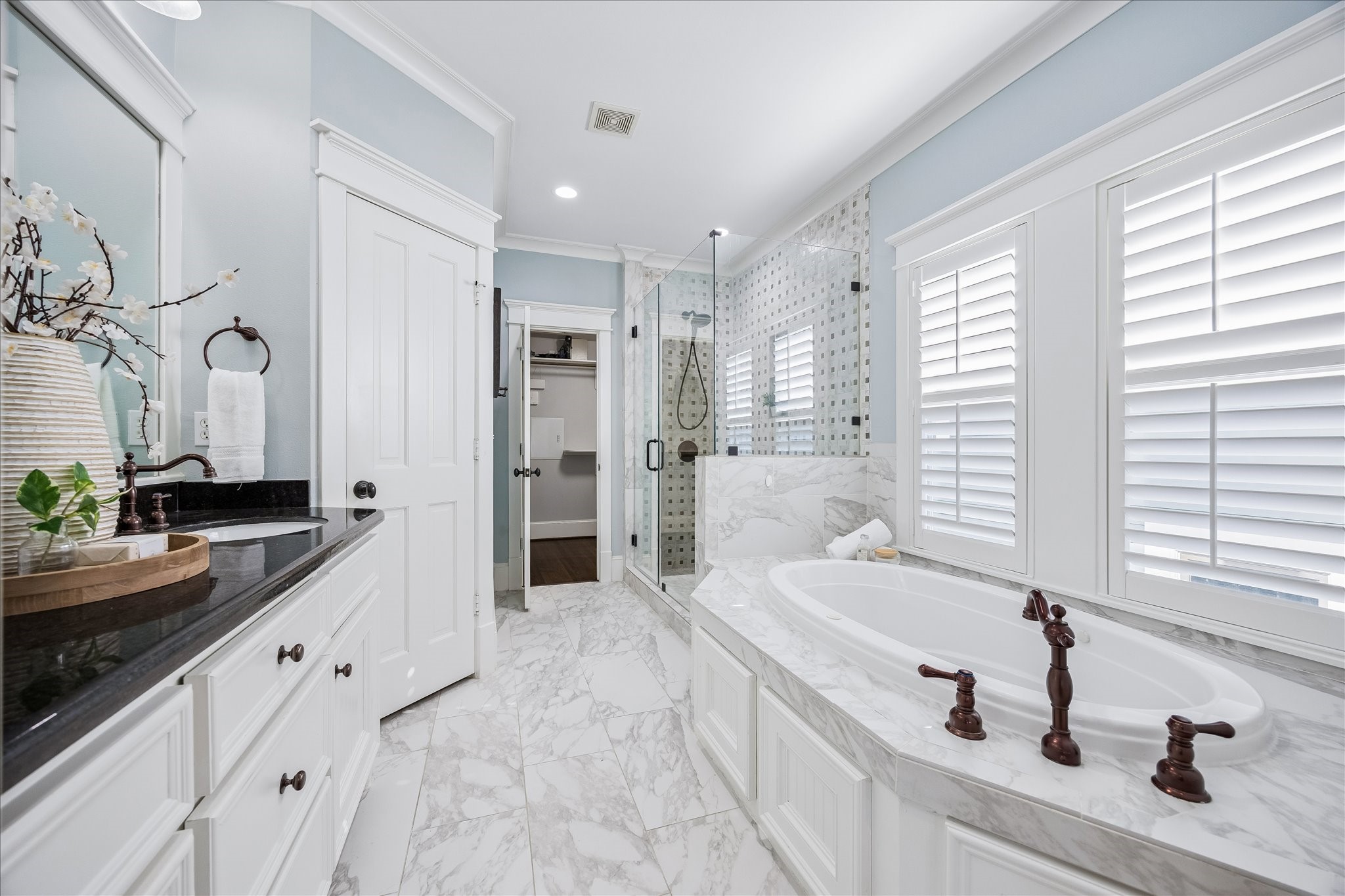 634 West 17th Street Houston, TX 77008 - Photo 20 of 42 The marble-wrapped primary bathroom offers a luxurious everyday escape, with a dual sink vanity, granite counters, full-width framed mirrors, stylish lighting, a deep jetted tub, and a frameless glass walk-in shower.