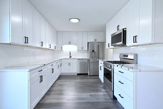 a kitchen with stainless steel appliances granite countertop a stove top oven a sink dishwasher and a refrigerator with wooden floor