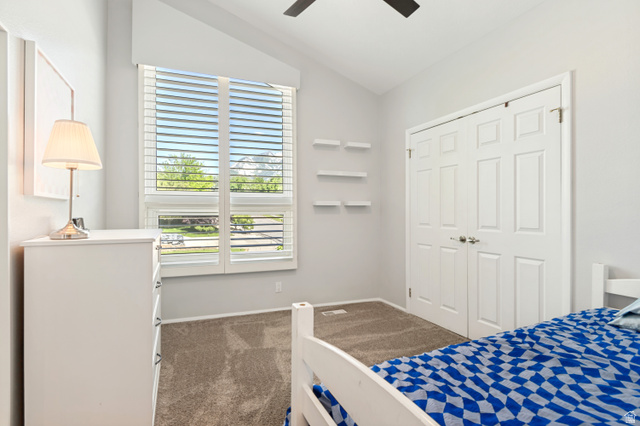 9832 Falconhurst Drive Sandy, UT 84092 - Photo 17 of 29 Vaulted ceiling bedroom featuring a large window with white plantation shutters, neutral tone carpet flooring, white bi-fold closet doors, and three white floating wall shelves