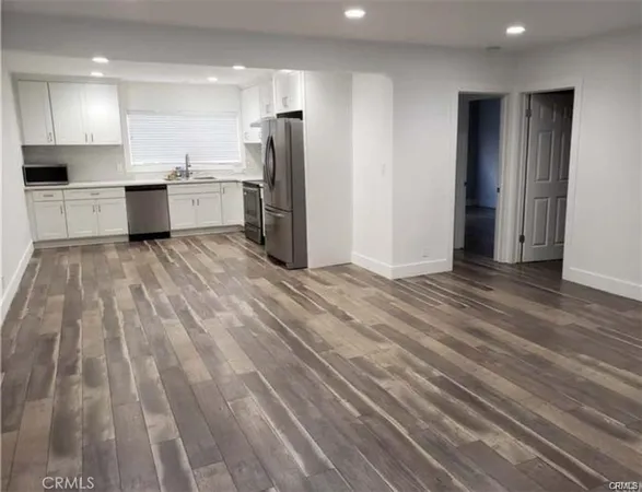 an empty room with stainless steel appliances wooden floor and view living room