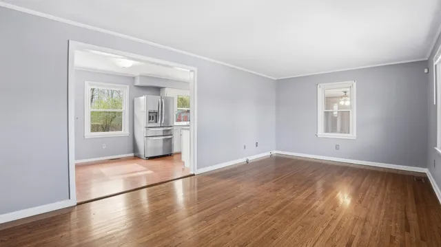 a view of an empty room with wooden floor and a window