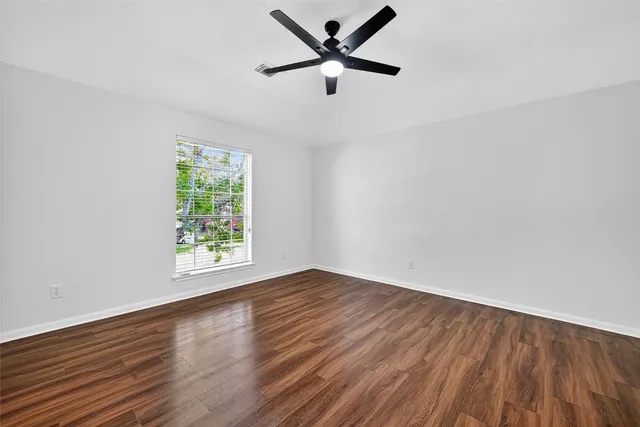 an empty room with wooden floor ceiling fan and windows