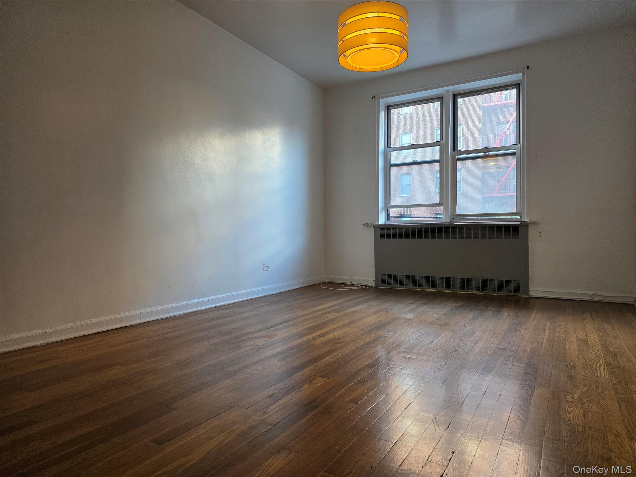 65-70 Booth Street, Unit 2B Queens, NY 11374 - Photo 4 of 8 an empty room with wooden floor and windows