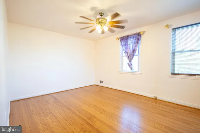 an empty room with wooden floor chandelier fan and windows