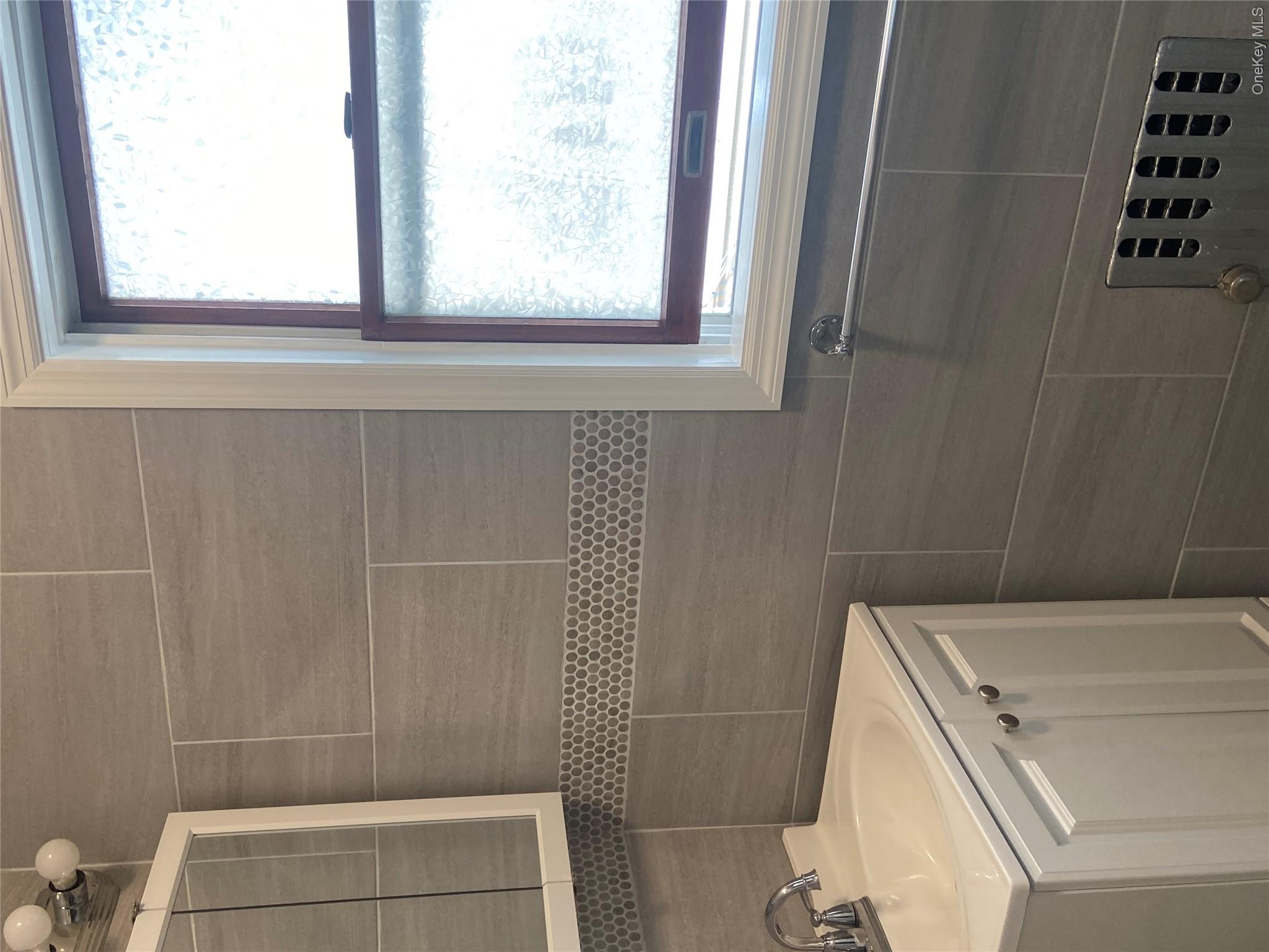 85-15 85th Street, Unit 2 Queens, NY 11421 - Photo 11 of 22 Bathroom featuring large format gray wall tiling with a mosaic accent band, a white vanity with integrated sink, chrome faucet, and a window with frosted glass