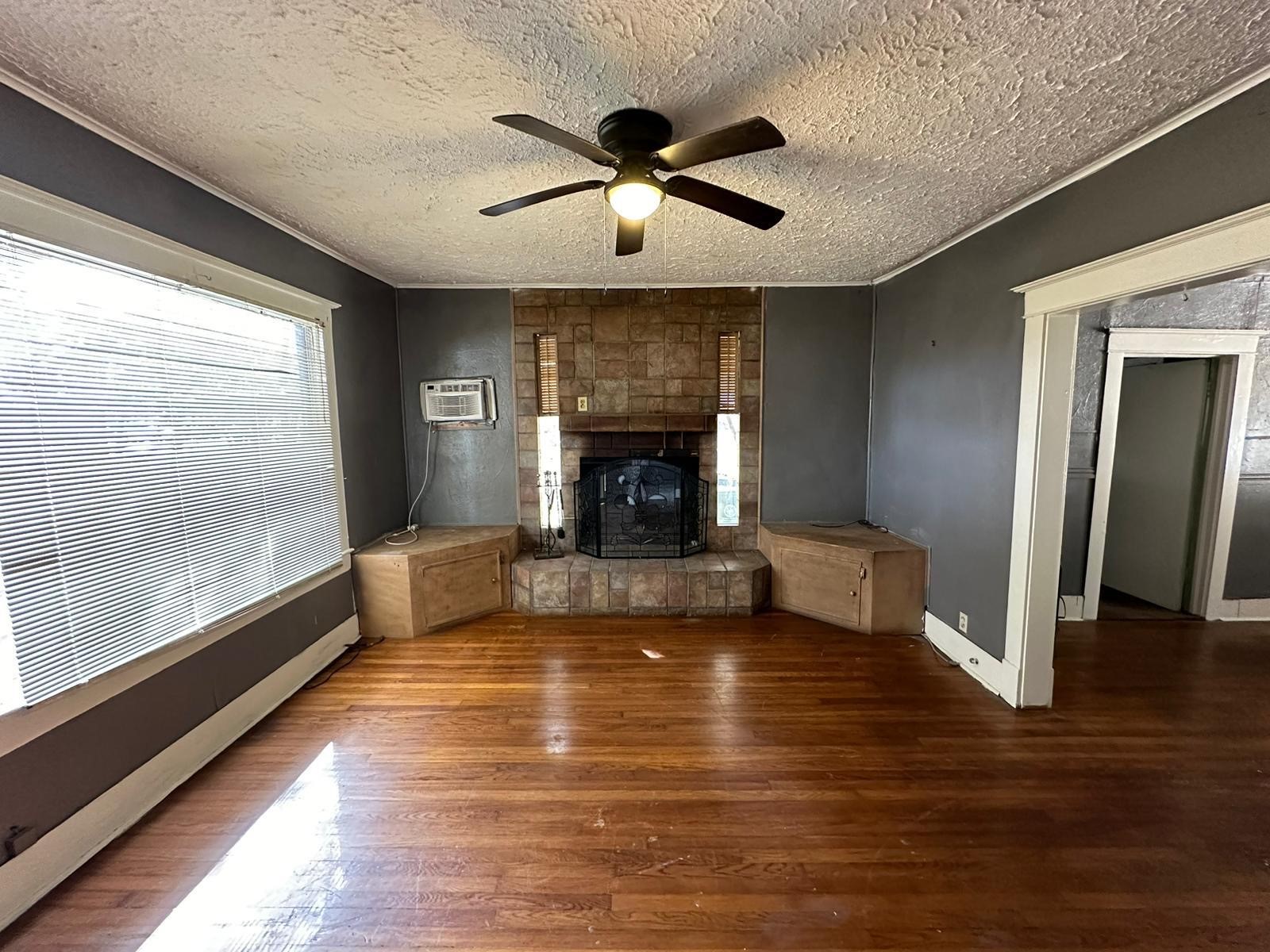 Spacious living room featuring a cozy fireplace, warm wood-inspired flooring, and abundant natural light