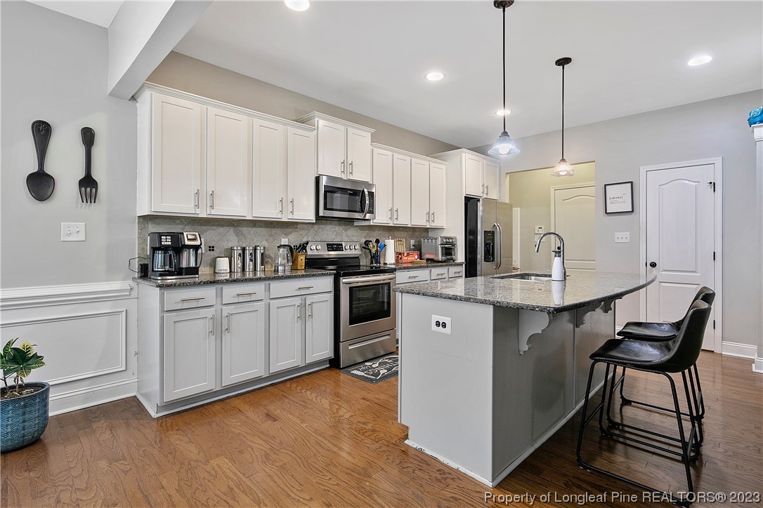 164 Valley Stream Road Spring Lake, NC 28390 - Photo 13 of 49 a kitchen with kitchen island granite countertop a stove a sink a microwave a dining table and chairs with wooden floor