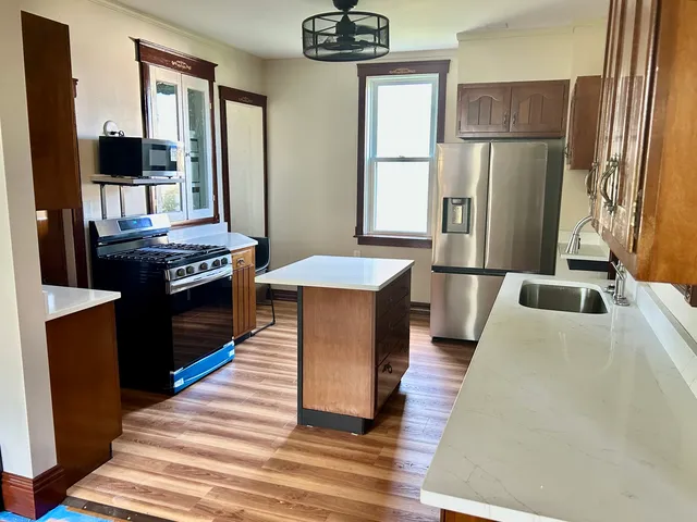 a kitchen with stainless steel appliances granite countertop a refrigerator a stove and a sink with wooden floor