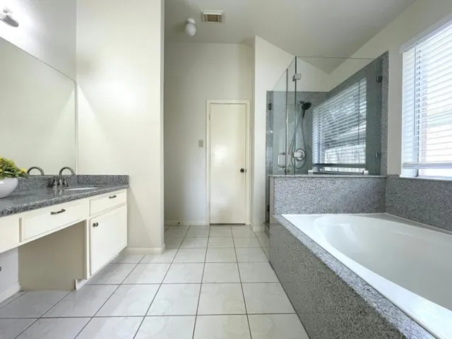 a spacious bathroom with a granite countertop sink a mirror and a bathtub