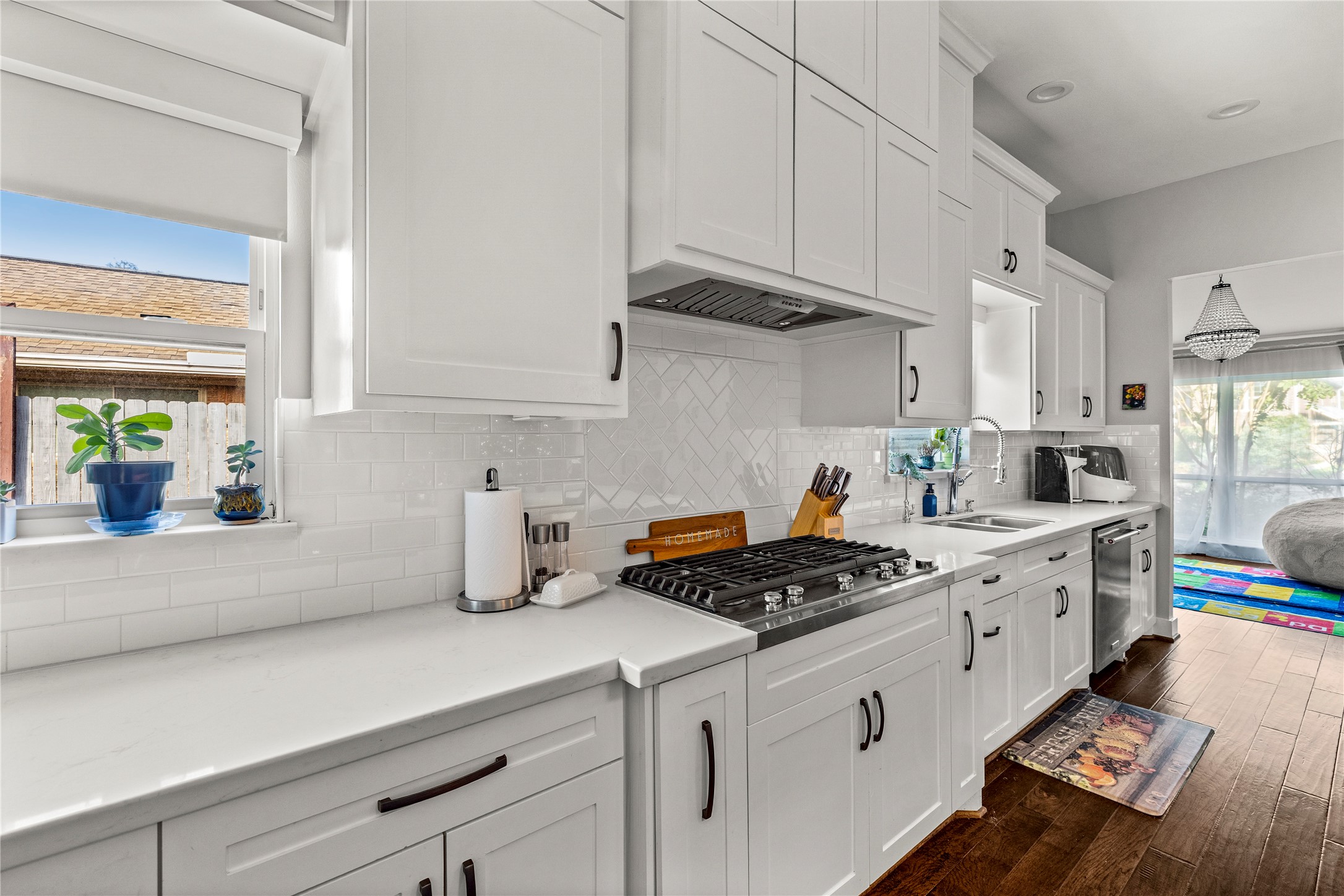 8422 Academy Street Houston, TX 77025 - Photo 16 of 47 Sleek, updated kitchen featuring pristine white cabinetry, quartz countertops, a gas cooktop with custom vent hood, and a beautiful herringbone tile backsplash. Abundant storage, modern hardware, and a large window add brightness and functionality to this stylish culinary space.
