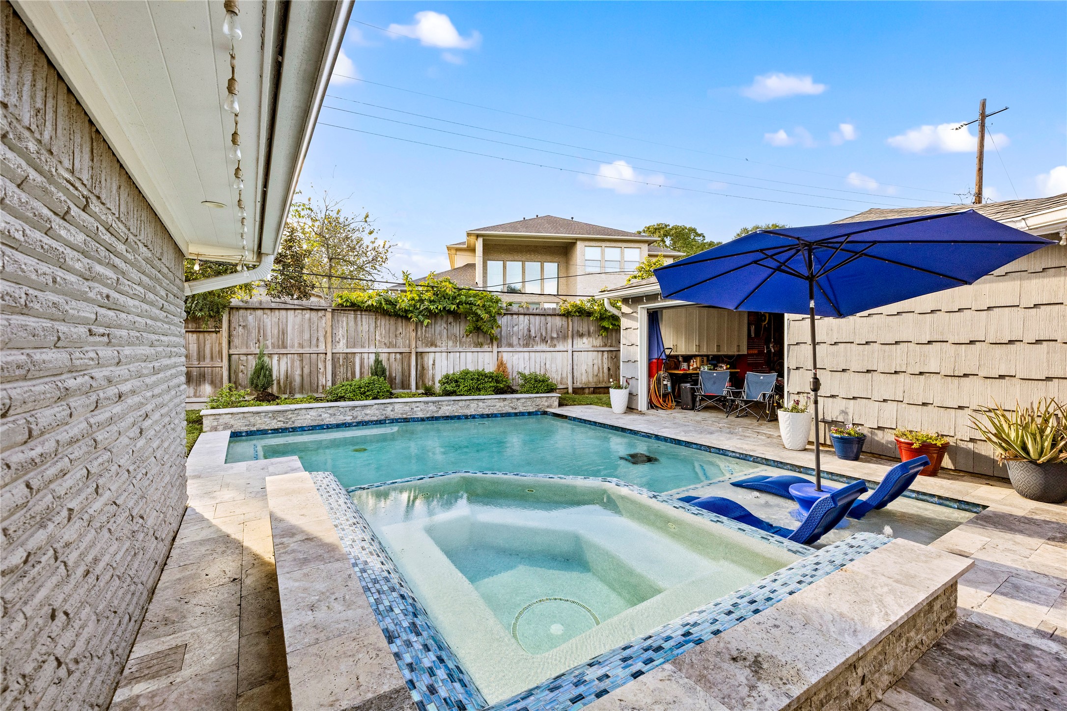 8422 Academy Street Houston, TX 77025 - Photo 25 of 47 Another angle of the backyard oasis showcasing the raised spa, sun shelf with loungers, and spacious pool deck. The surrounding landscaping and open patio provide the ideal setting for outdoor dining, entertaining, and relaxation.