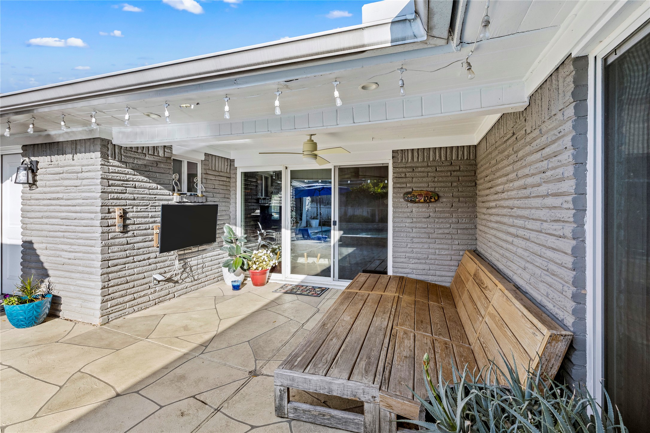 8422 Academy Street Houston, TX 77025 - Photo 34 of 47 Additional view of the covered patio featuring a mounted TV, ceiling fan, and bench seating. This spacious outdoor area provides seamless access to the pool and is perfect for entertaining or relaxing year-round.