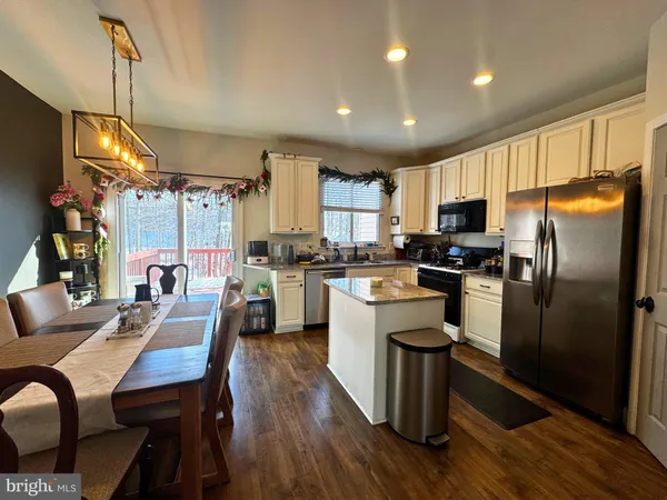 a kitchen with kitchen island a refrigerator a stove a sink dishwasher a dining table and chairs with wooden floor