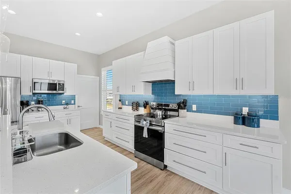 a kitchen with a sink dishwasher stove and white cabinets with wooden floor