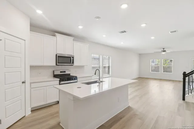 a kitchen with stainless steel appliances a stove a sink a refrigerator white cabinets and wooden floor