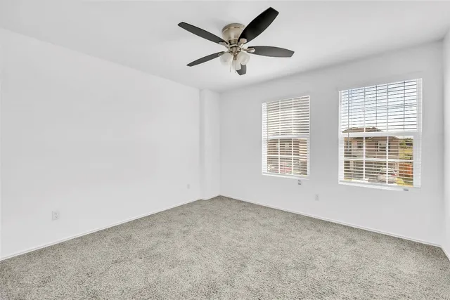 an empty room with ceiling fan and windows
