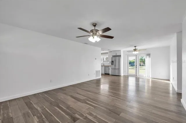 a view of an empty room with wooden floor and a ceiling fan