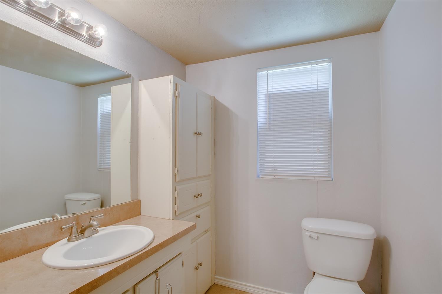 3114 30th Street Lubbock, TX 79410 - Photo 17 of 19 a bathroom with a toilet a sink a mirror and a shower