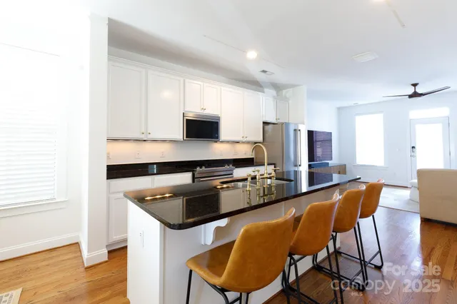 a kitchen with stainless steel appliances granite countertop a stove a refrigerator a sink dishwasher and white cabinets with wooden floor