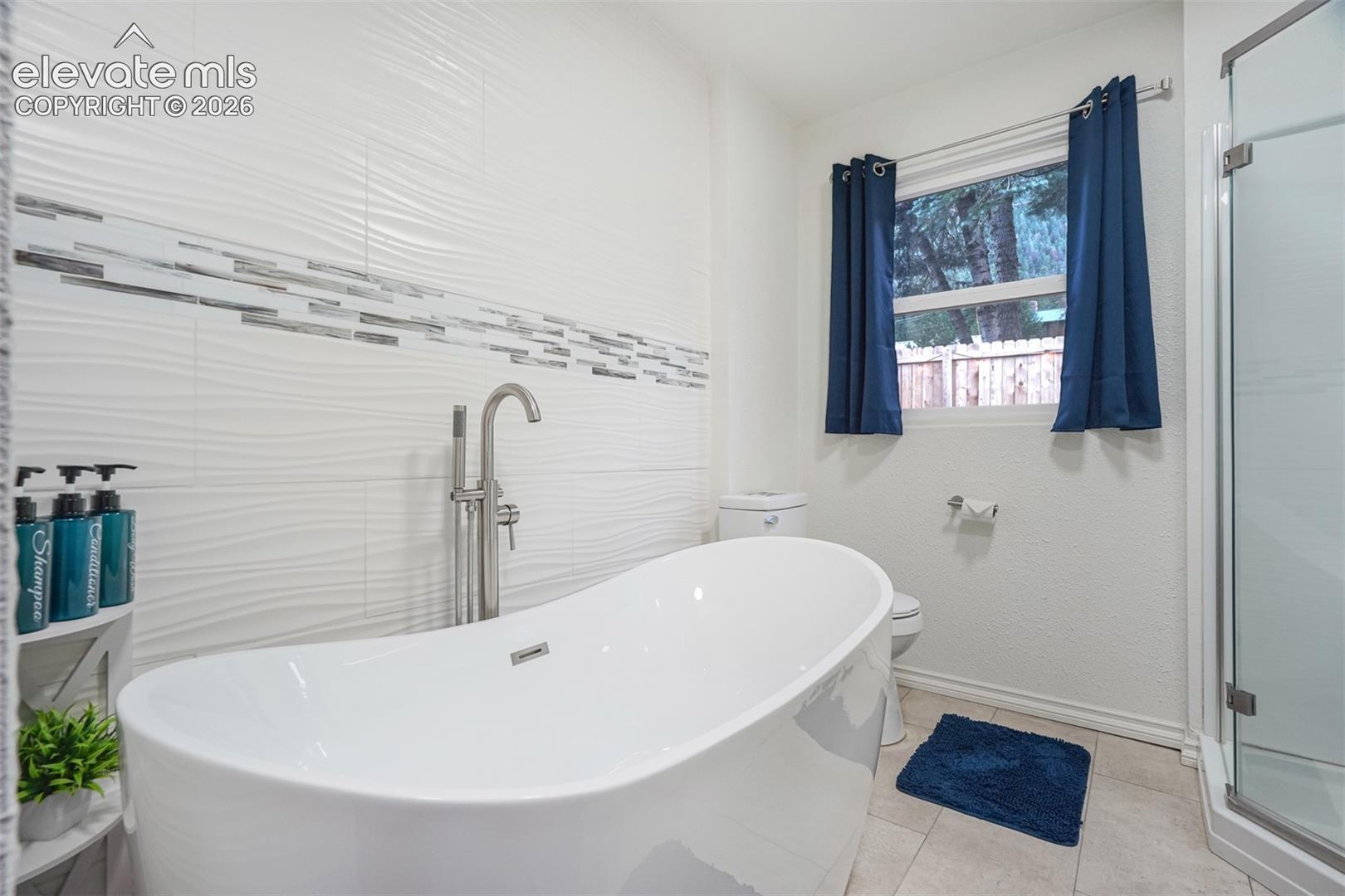 9955 Mesa Road Cascade, CO 80809 - Photo 23 of 41 Freestanding soaking tub with floor-mounted faucet, textured tile wall with decorative mosaic accent, and glass-enclosed shower