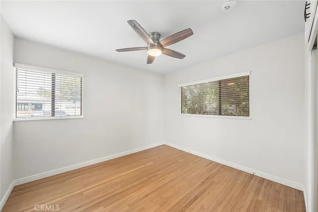 a view of an empty room with wooden floor and a ceiling fan