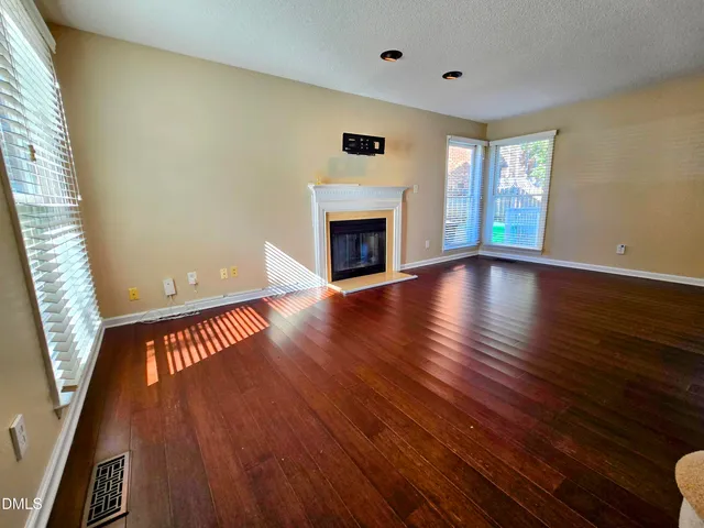a view of an empty room with wooden floor fireplace and a window