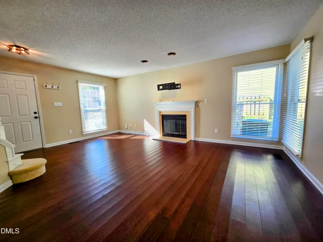 an empty room with wooden floor fireplace and windows