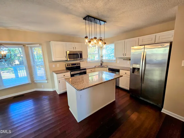 a kitchen with a refrigerator a sink dishwasher a stove and a dining table with wooden floor