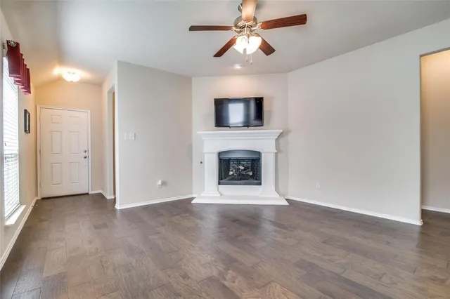 an empty room with wooden floor a ceiling fan a fireplace and windows