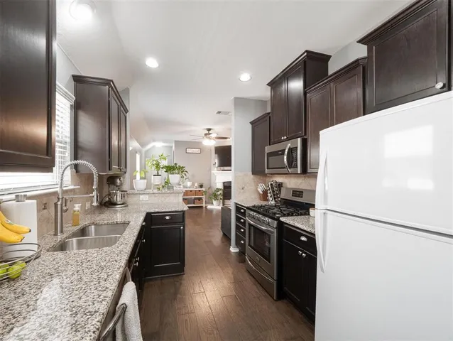 a kitchen with granite countertop a refrigerator a sink a stove and cabinets