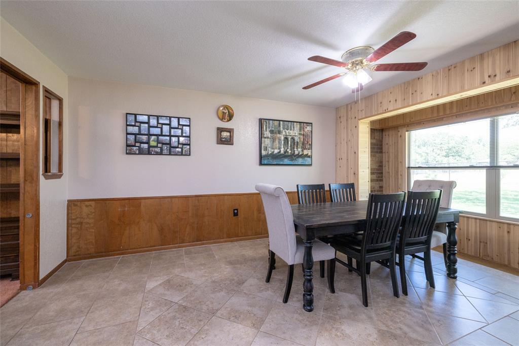 151 County Road 3699 Springtown, TX 76082 - Photo 9 of 35 Spacious dining area featuring neutral tile flooring, a prominent window with a wood-paneled surround, and a ceiling fan with integrated lighting