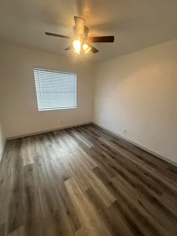 an empty room with wooden floor chandelier fan and windows