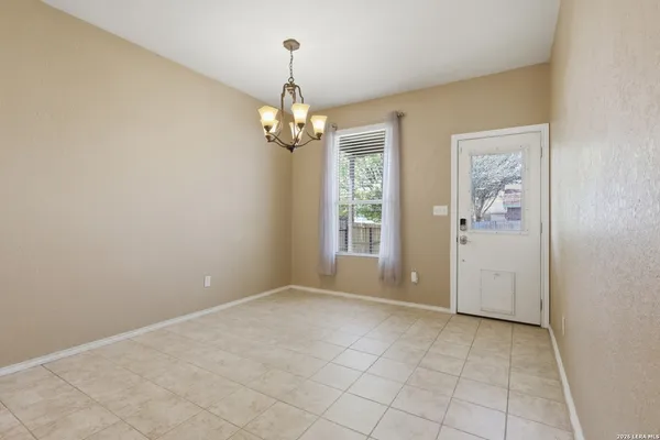 an empty room with chandelier fan and kitchen view