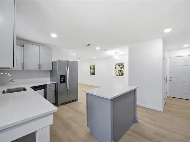 a kitchen that has a refrigerator a sink and white cabinets with wooden floor
