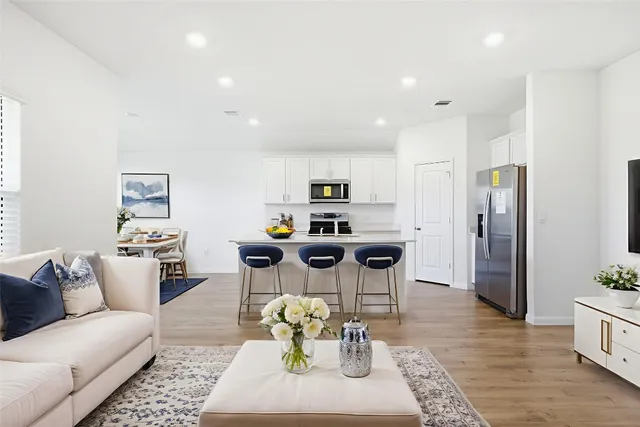 a living room with stainless steel appliances furniture a rug and a kitchen view