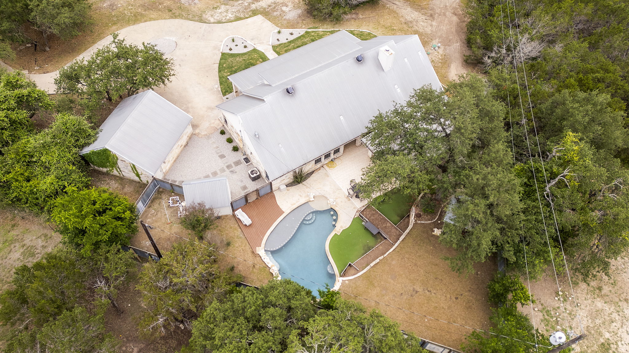 1129 Cedar Pass Road Driftwood, TX 78619 - Photo 39 of 40 From directly above, you can see the unique shape of the pool, featuring a large tanning ledge and built-in bar stools. It’s perfectly framed by the travertine patio and those lush green turf accents we saw earlier.