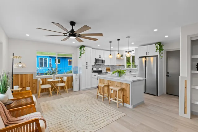 a kitchen with stainless steel appliances kitchen island granite countertop a refrigerator a stove a sink a dining table and chairs with wooden floor
